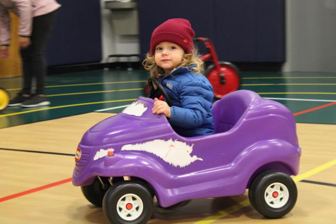 Child in foot powered purple car moving around the gym