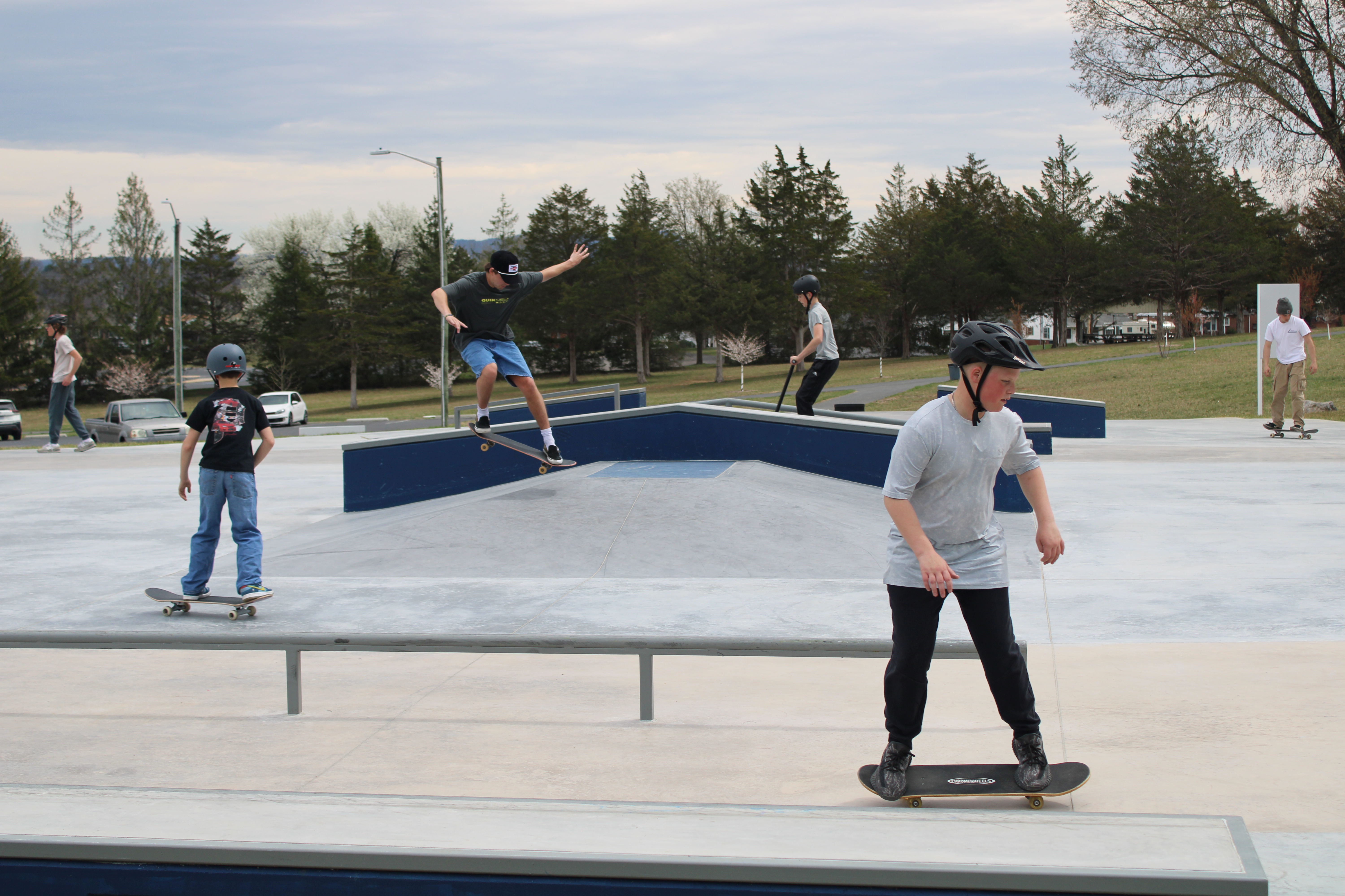multiple people riding skateboards and scooters at the skatepark.