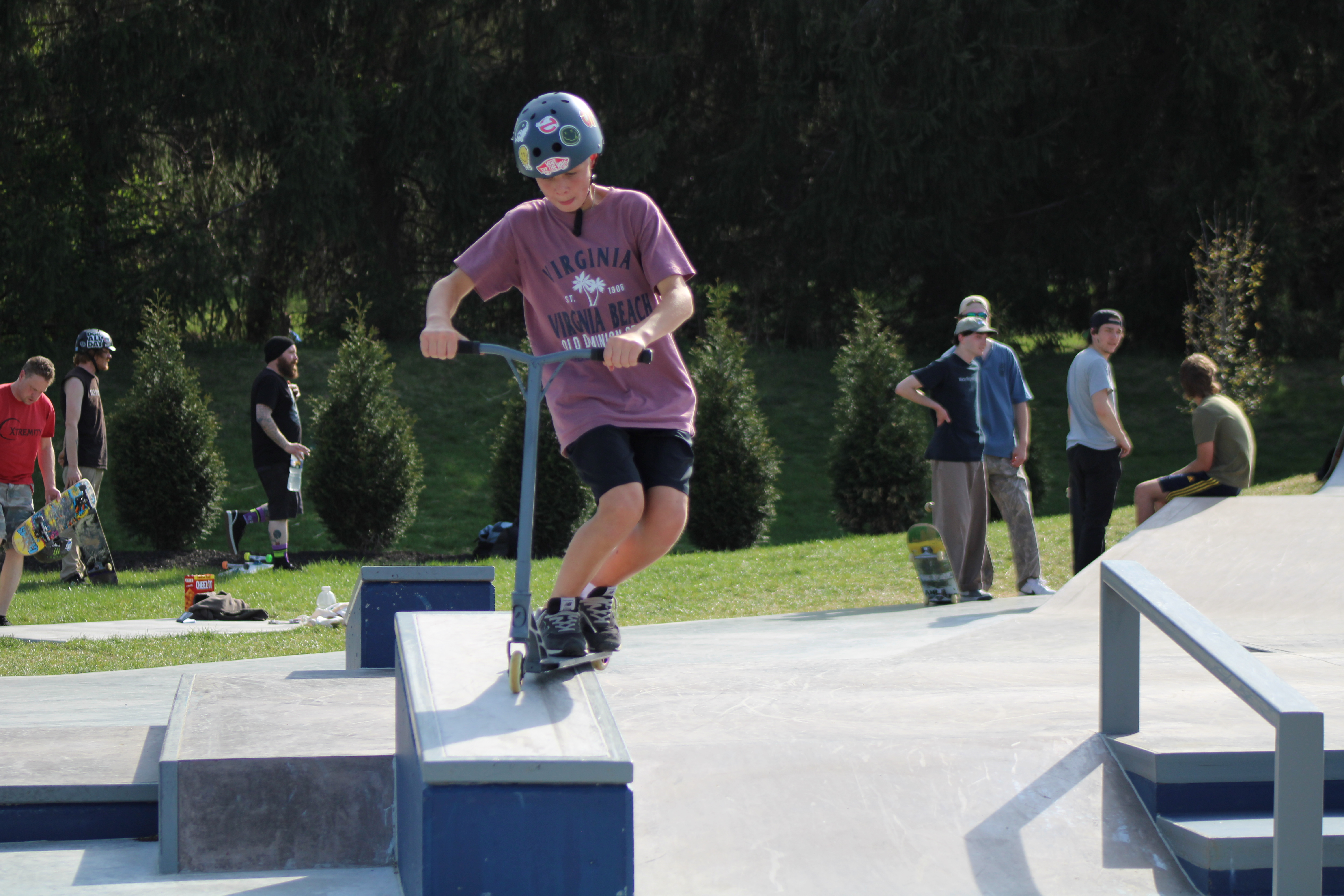 Image of a child riding a scooter along a ledge at the skate park